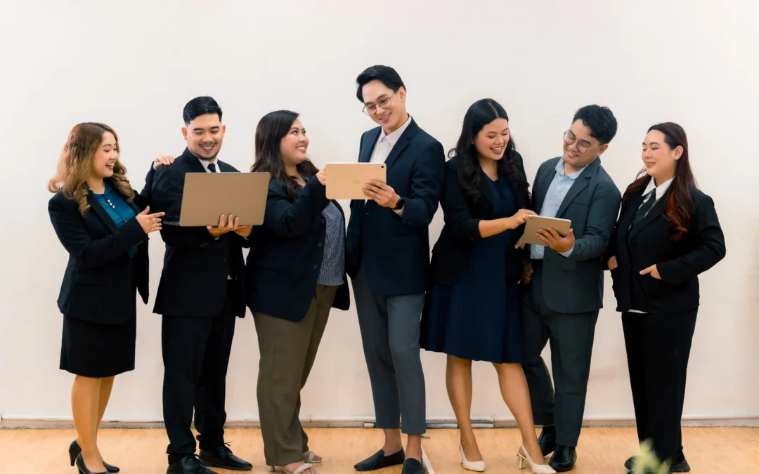 A diverse professional team standing in a bright office collaborating with a laptop and tablets