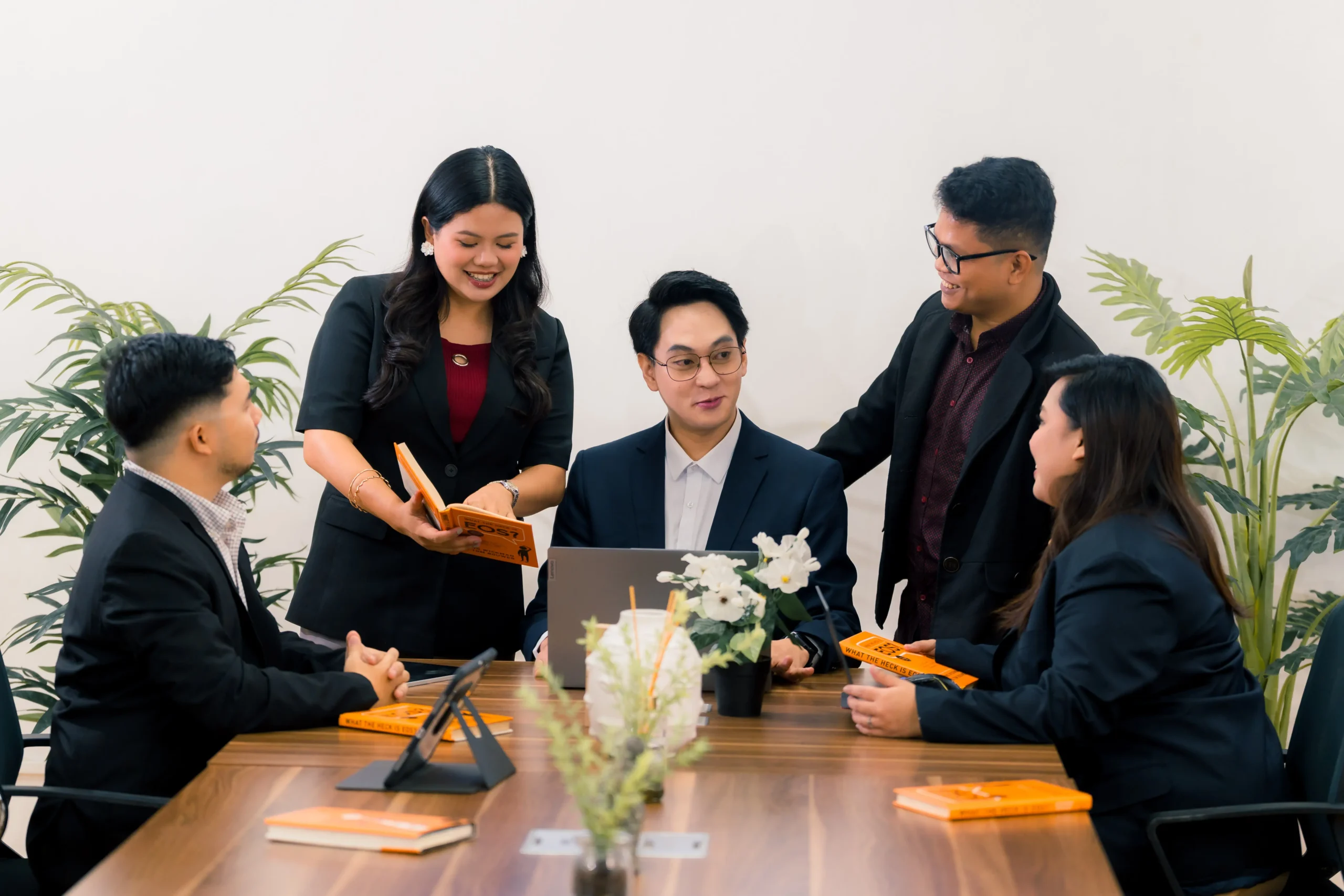 A professional team in business attire having a collaborative meeting around a conference table with books and a laptop