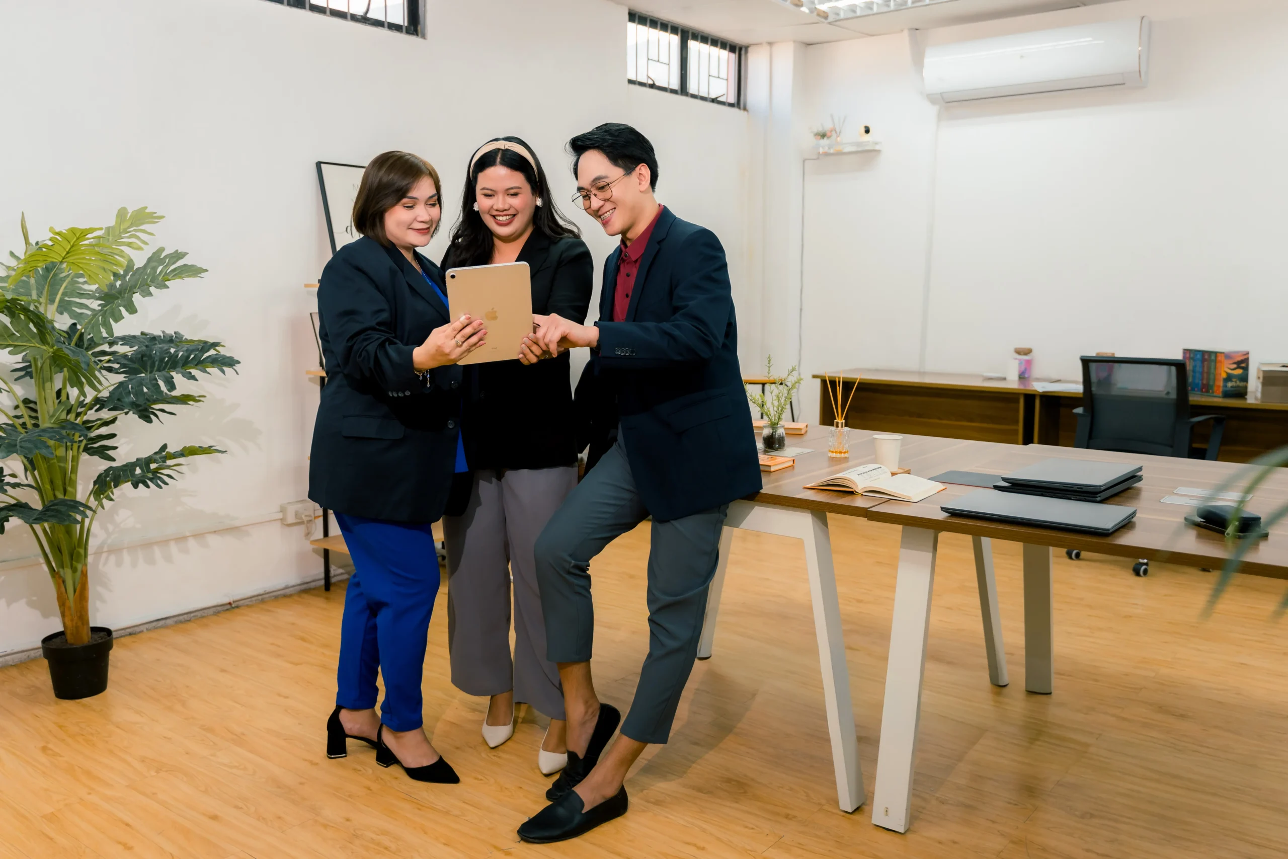 Three professional colleagues in a bright, modern office collaborating on a tablet together