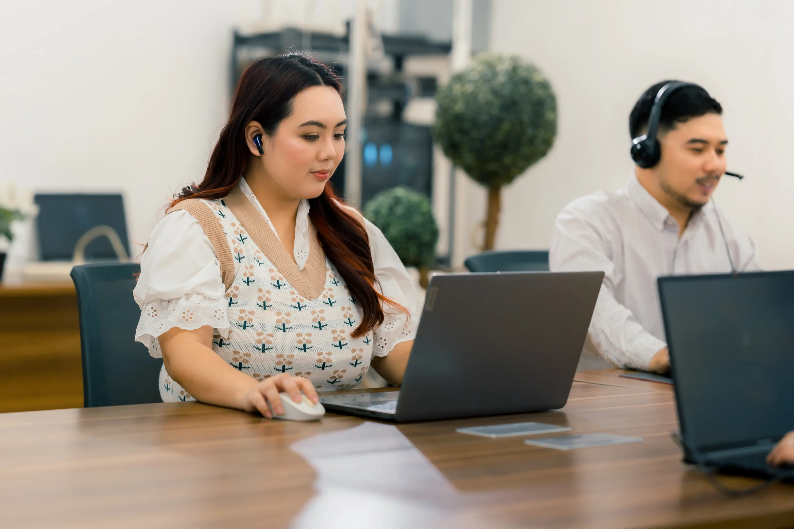 Two corporate employees wearing headsets and using laptops while working in a modern office
