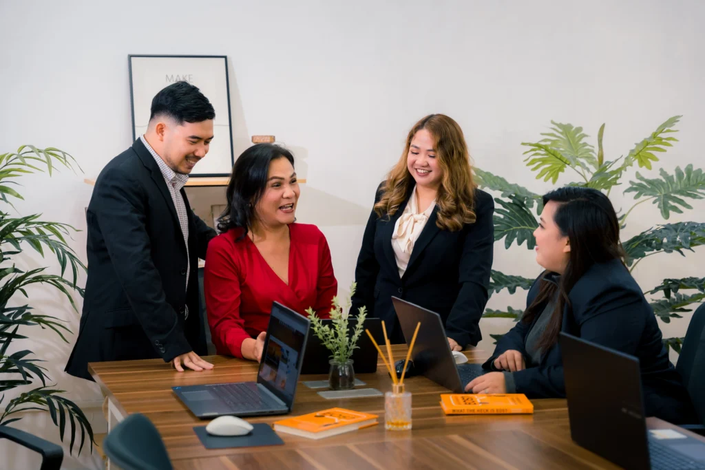 A diverse team of professionals happily collaborating around a conference table with laptops.